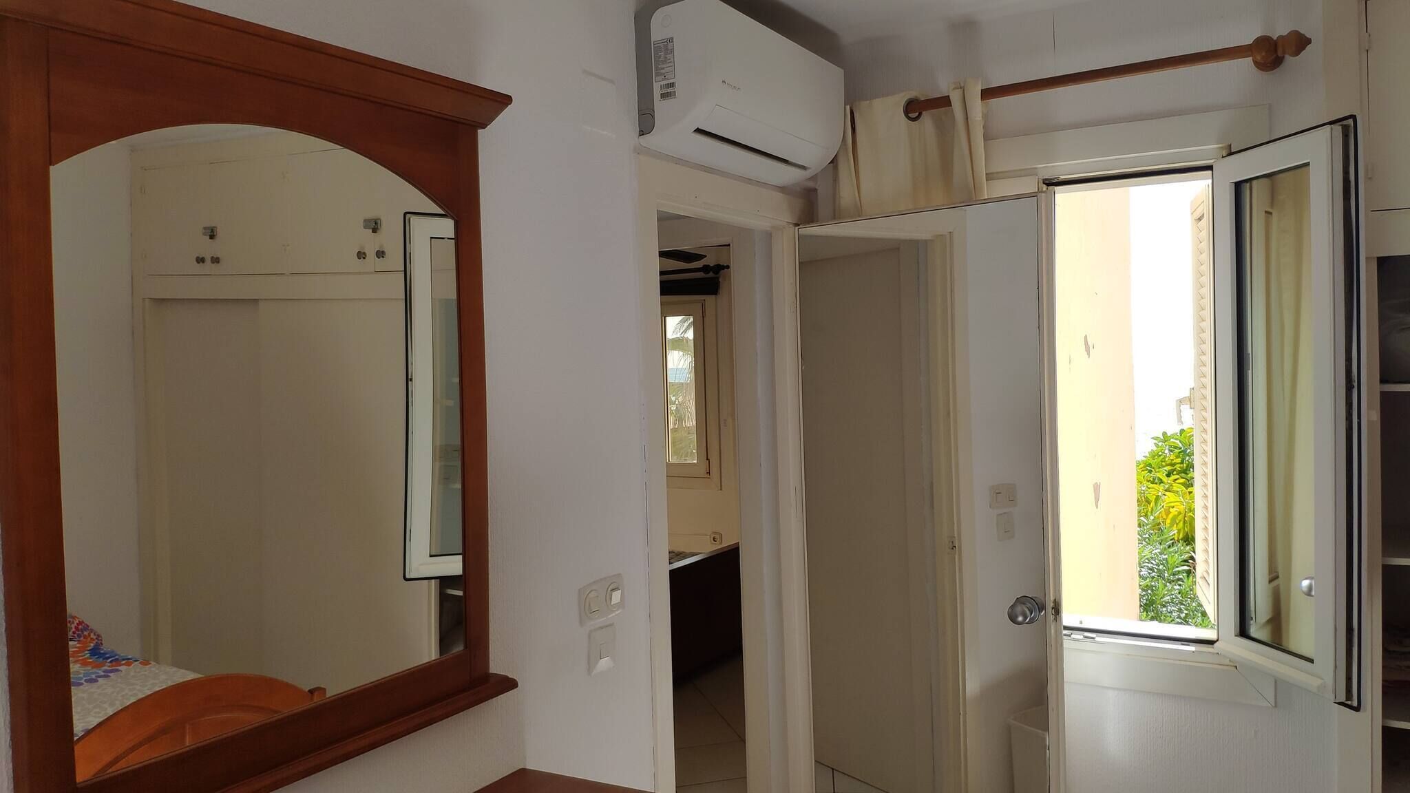A hallway with a wooden-framed mirror, a white door, and an air conditioning unit mounted on the wall.
