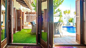 Habitación con vista a una piscina, un patio con mobiliario exterior y un césped verde.