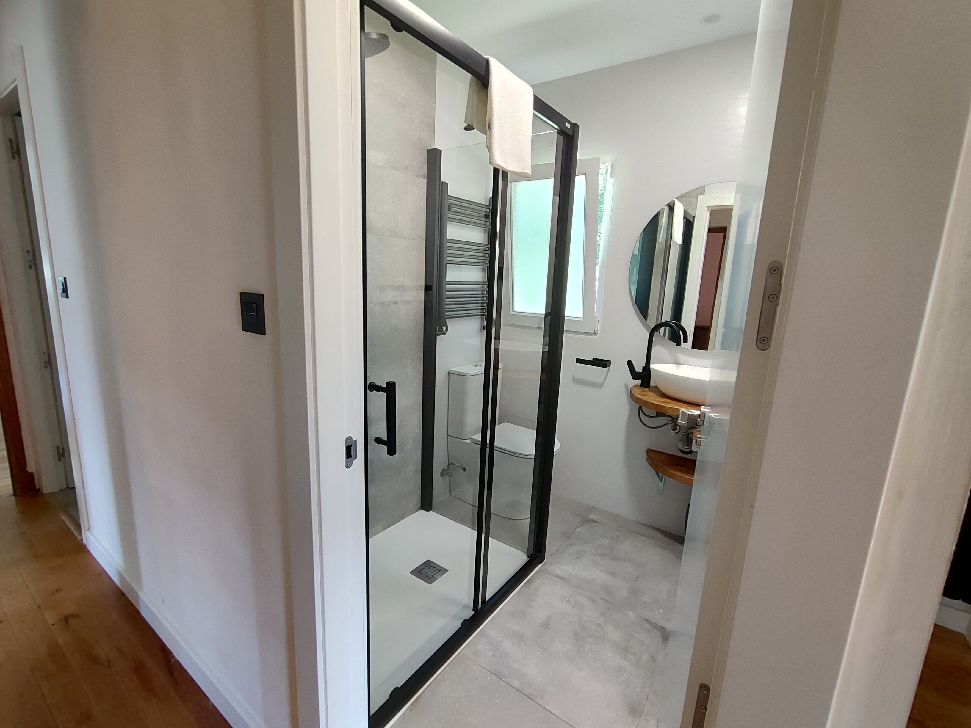A modern bathroom with a glass shower enclosure, a white sink with a wooden countertop, and a large mirror above the sink.