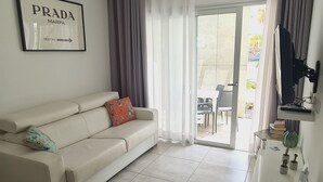 A modern living room with a white sofa, a ceiling fan, and a large window with curtains. - Luminoso Bilocale Vicino Al Mare (La Oliva)
