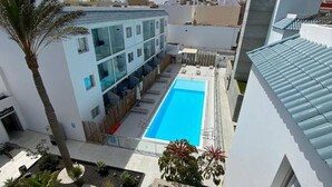 A modern building with a swimming pool, surrounded by greenery and palm trees. - Luminoso Bilocale Vicino Al Mare (La Oliva)