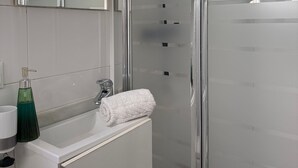 A modern bathroom with a glass shower enclosure, a white sink with a soap dispenser, and a towel. - Beach House Apartment (Mairena del Aljarafe)
