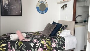 A bedroom with a bed, a small desk, a kitchen area, and a wall-mounted shelf. - Beach House Apartment (Mairena del Aljarafe)