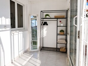 A hallway with a white door, a black metal shelf unit with baskets and a potted plant, and a window with a view of greenery. - Charming House With Nature (Torrevieja)