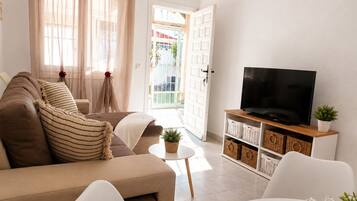 Una sala de estar con un sofá, un televisor sobre un mueble de madera y una mesita con una planta.