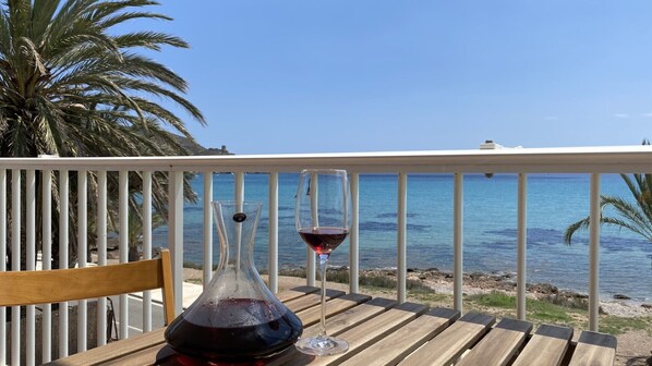 A wooden table with a bottle of red wine and a wine glass on a balcony overlooking a beach with palm trees and the sea. - Apartament In Fron Of The Sea (Cartagena)