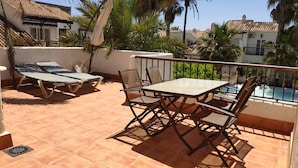 En terrasse med et bord og stole, liggestol og udsigt til en swimmingpool.