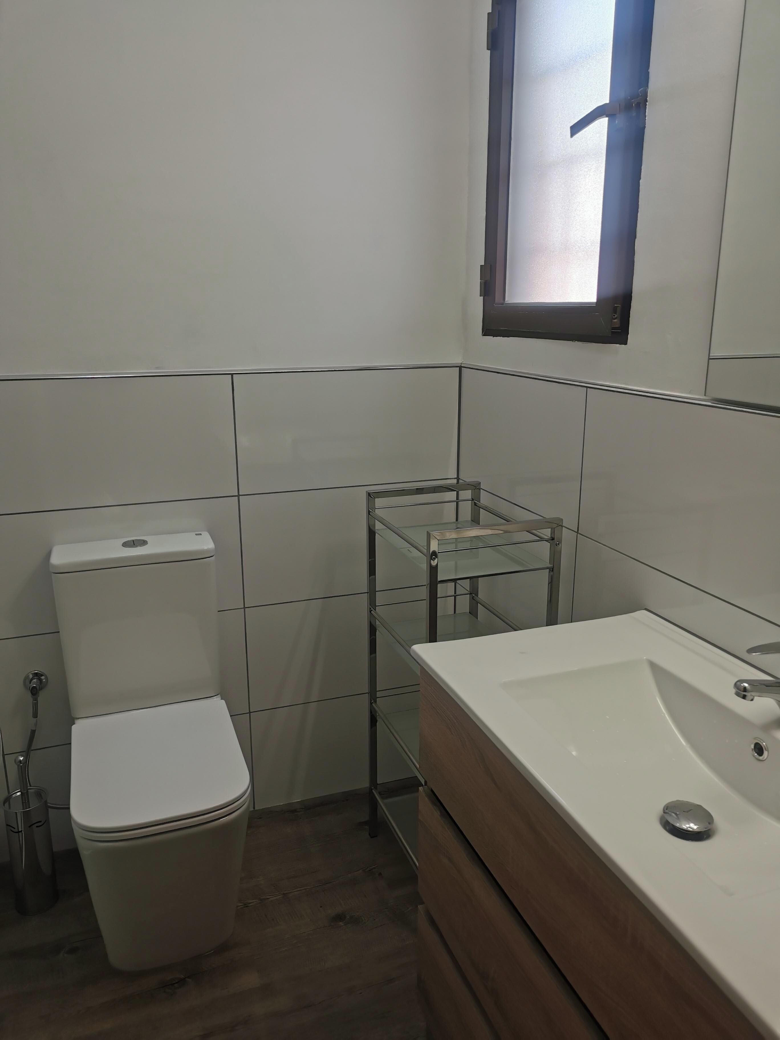 Un baño con inodoro, estante de vidrio y lavamanos con espejo.
