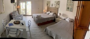 A hotel room with two beds, a dining table with chairs, and a small table with a basket and remote controls. - Sunny Apartment at Benal Beach Resort 4 Pools, Water Slides & Steps From Beach (Benalmádena)