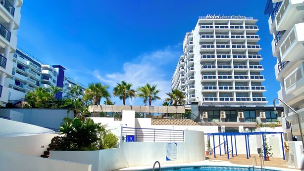 Un hotel con area piscina, palme e cielo azzurro.