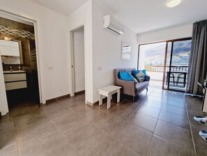 A modern living room with a grey sofa, a small white table, and a balcony with a view of the mountains. - 413 Cumana2 Puerto Rico By Alquiler de Sùeño (Mogan)