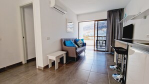A modern living room with a sofa, a small table, and a kitchen area with a TV. - 413 Cumana2 Puerto Rico By Alquiler de Sùeño (Mogan)