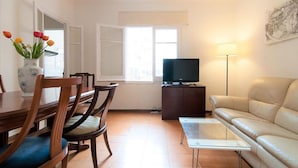 Una sala de estar con comedor, un sofá, un televisor sobre un mueble bajo y un florero con flores.