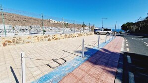 A paved area with a chain barrier, a white vehicle, and a road with a blue line. - 509 Cumana2 Puerto Rico By Alquiler de Sùeño (Mogan)