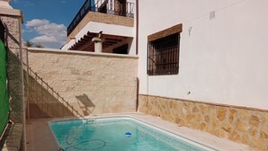 A swimming pool adjacent to a building with a stone wall and a window with metal bars.