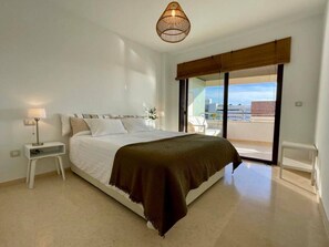 Una camera da letto moderna con un letto grande, un comodino con una lampada, vista sulla città tramite una porta scorrevole e una lampada a sospensione.