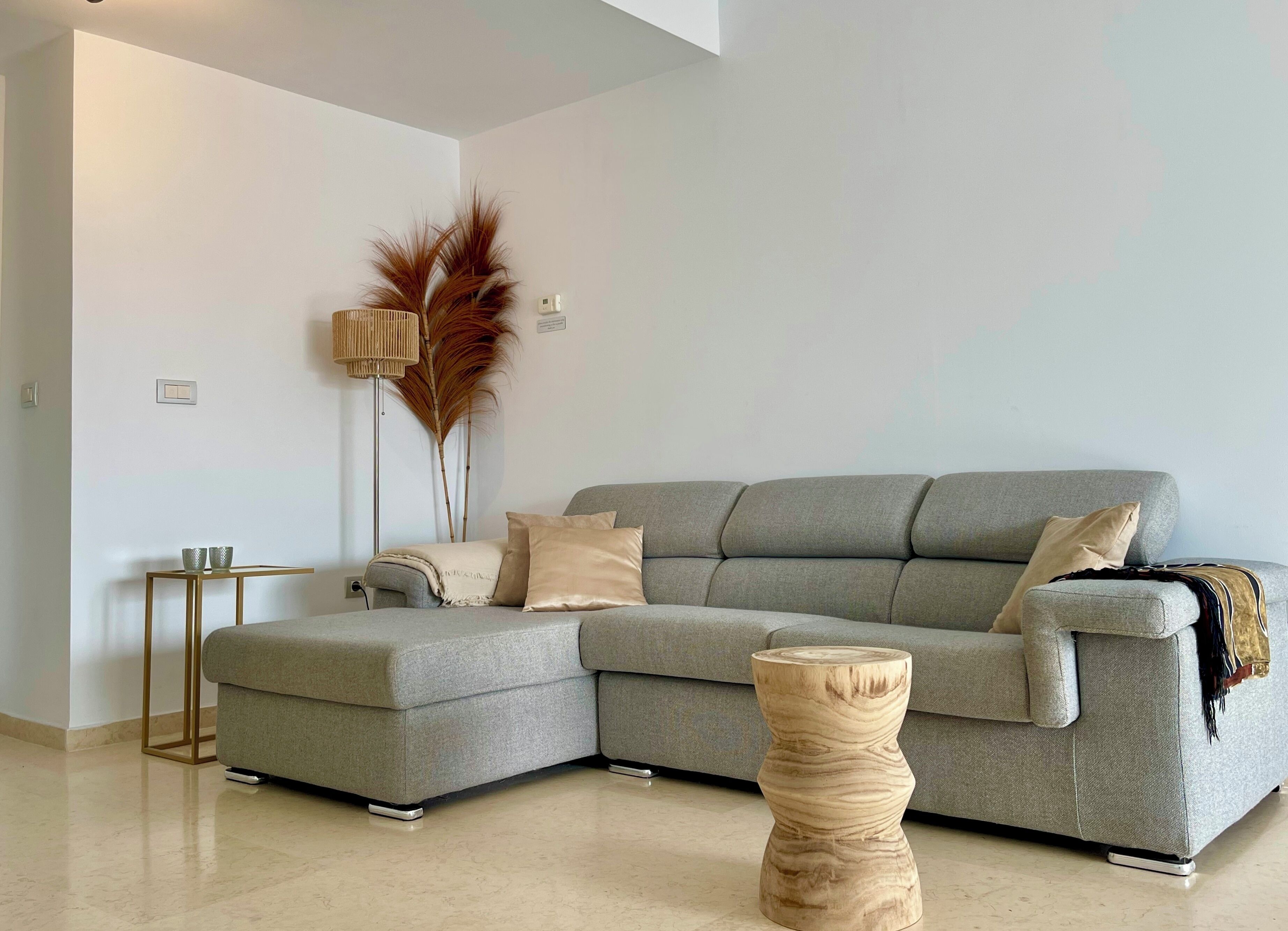 A modern living room with a grey sectional sofa, a small wooden side table, and a tall floor lamp with a woven shade.
