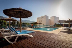 Area piscina con lettini e ombrelloni, cielo sereno e un edificio con la scritta "Palacio de Feria y Congresos Marbella".
