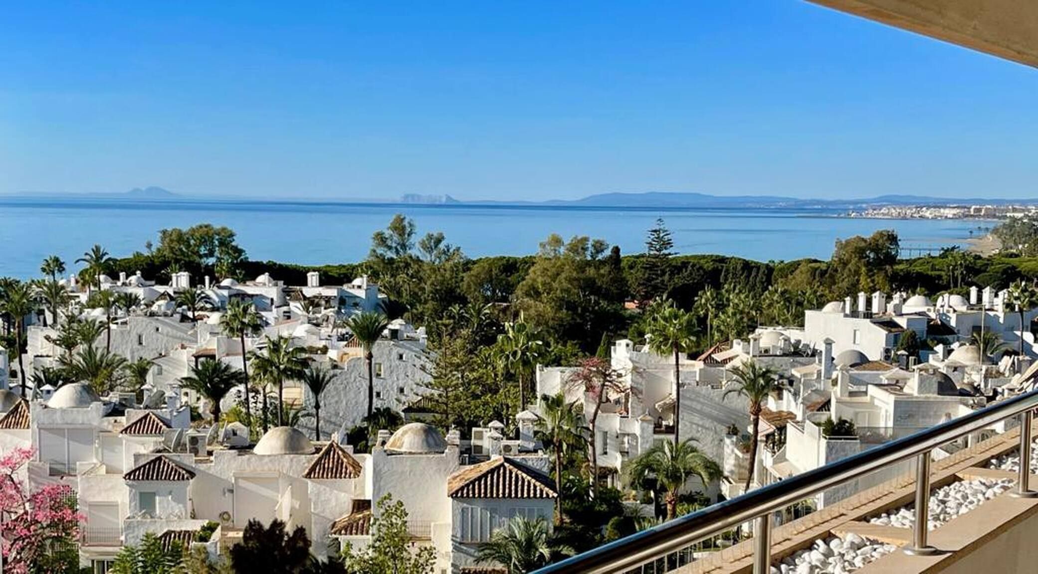 Ein Küstenort mit weißen Gebäuden, Palmen und freiem Blick auf das Meer.