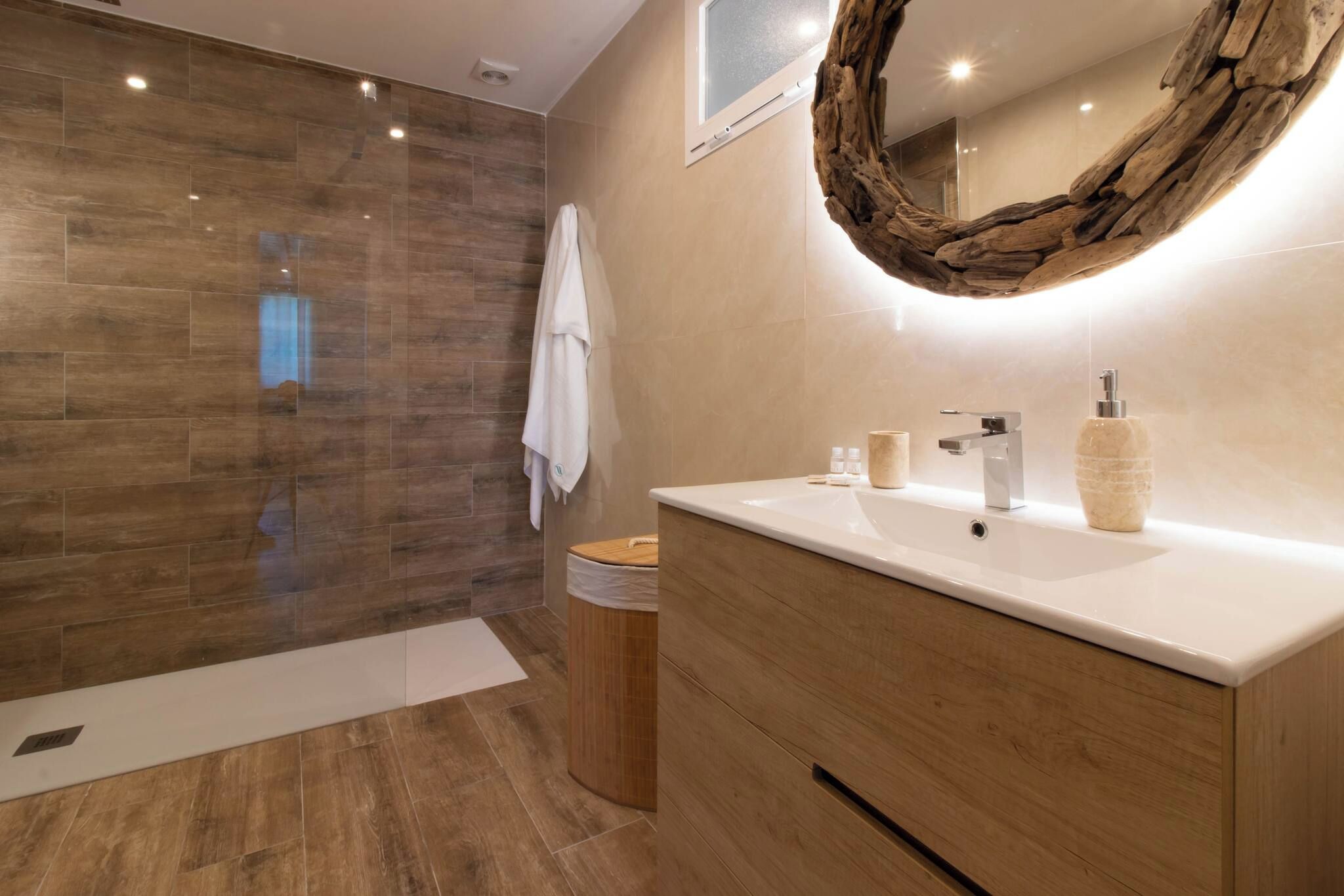 A modern bathroom with a wooden vanity, a large mirror, and a shower area with wooden flooring.