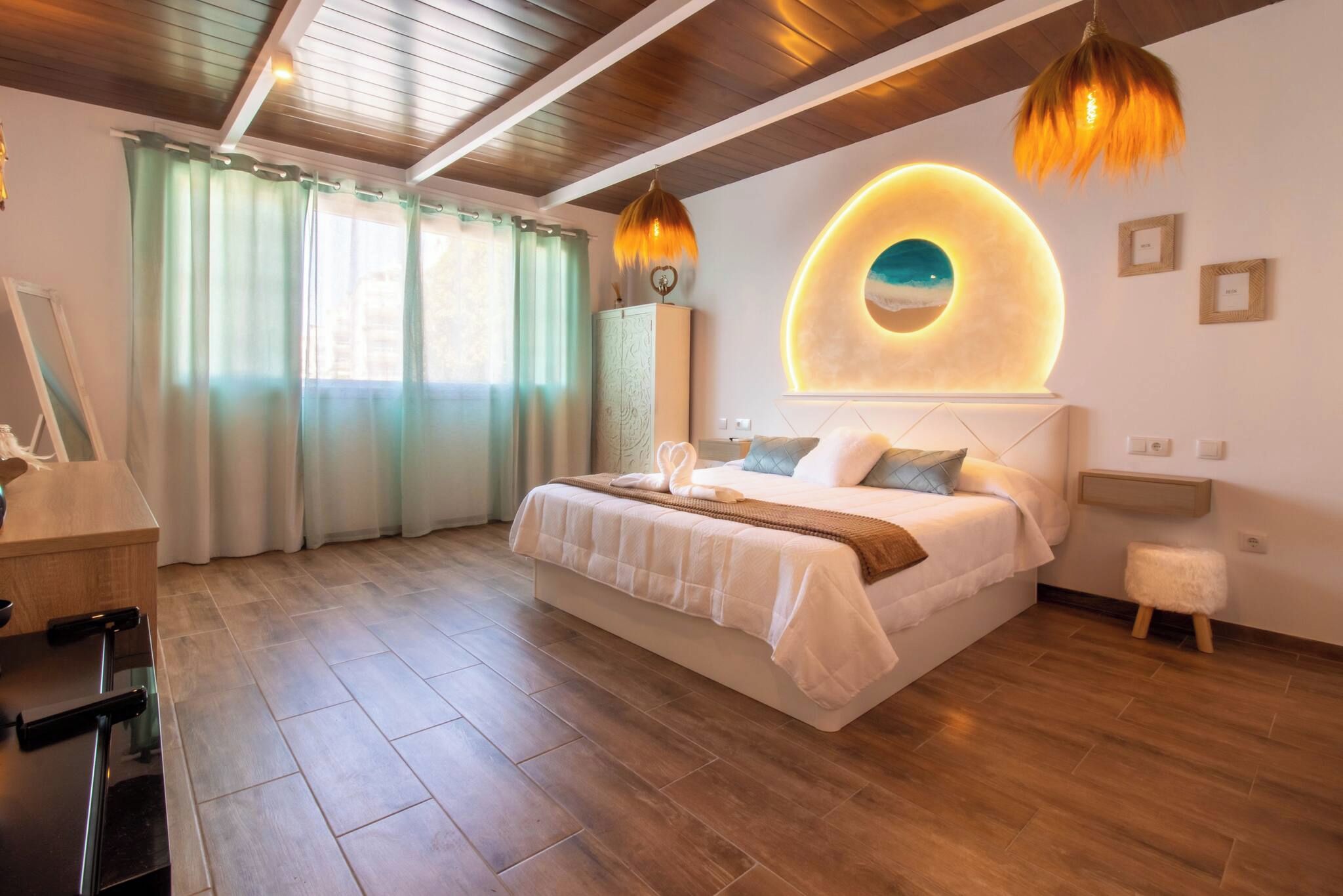 A modern bedroom with a large bed, wooden flooring, a circular wall feature, and a small stool.