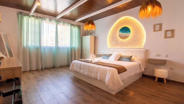 A modern bedroom with a large bed, wooden flooring, a circular wall feature, and a small stool. - Room in Guest Room - Private Room in the Fishing Port of Marbella (Marbella)