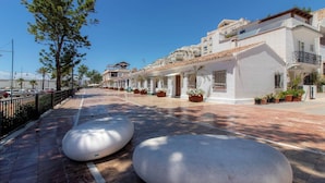 A paved walkway with large stone planters, white buildings with balconies, and a clear blue sky. - Room in Guest Room - Private Room in the Fishing Port of Marbella (Marbella)