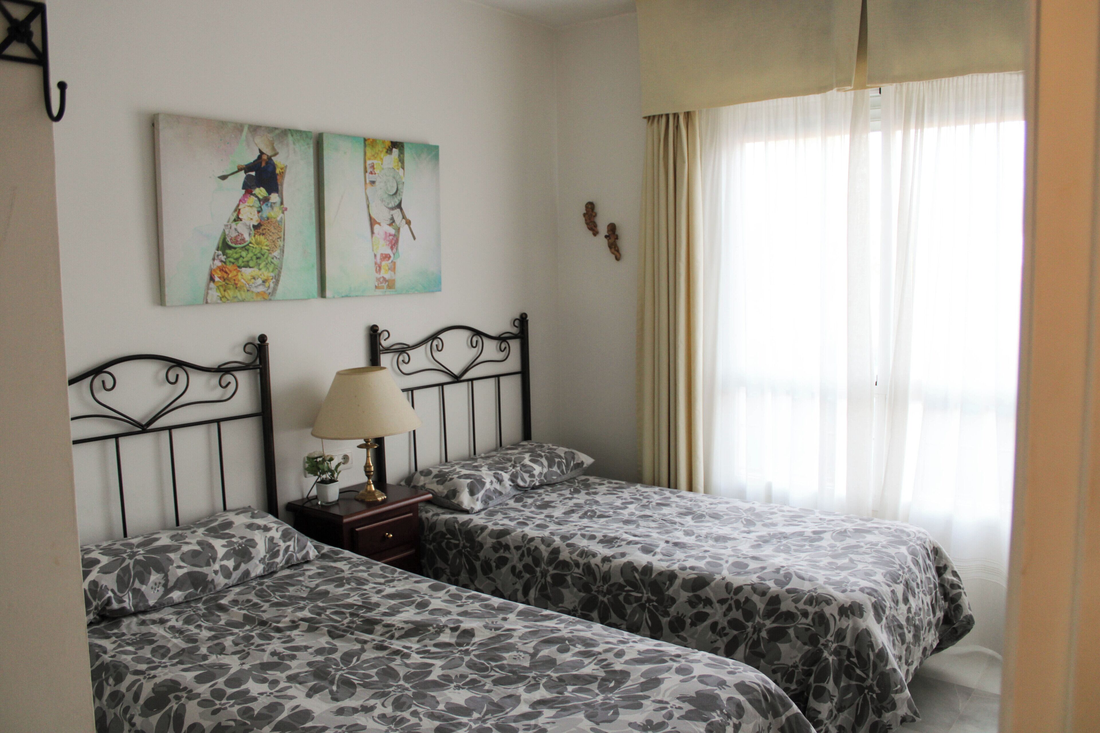 A room with two beds, a nightstand with a lamp, and two wall-mounted paintings.