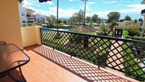 Ein Balkon mit Tisch und Stühlen, Blick auf eine Wohngegend mit Häusern und Grünflächen, und ein klarer Himmel.