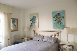 Une chambre à coucher comprenant un lit, deux tables de chevet, une chaise et des œuvres d’art accrochées aux murs.