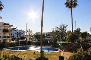 Une piscine entourée de palmiers et un bâtiment doté d’un toit en tuiles.