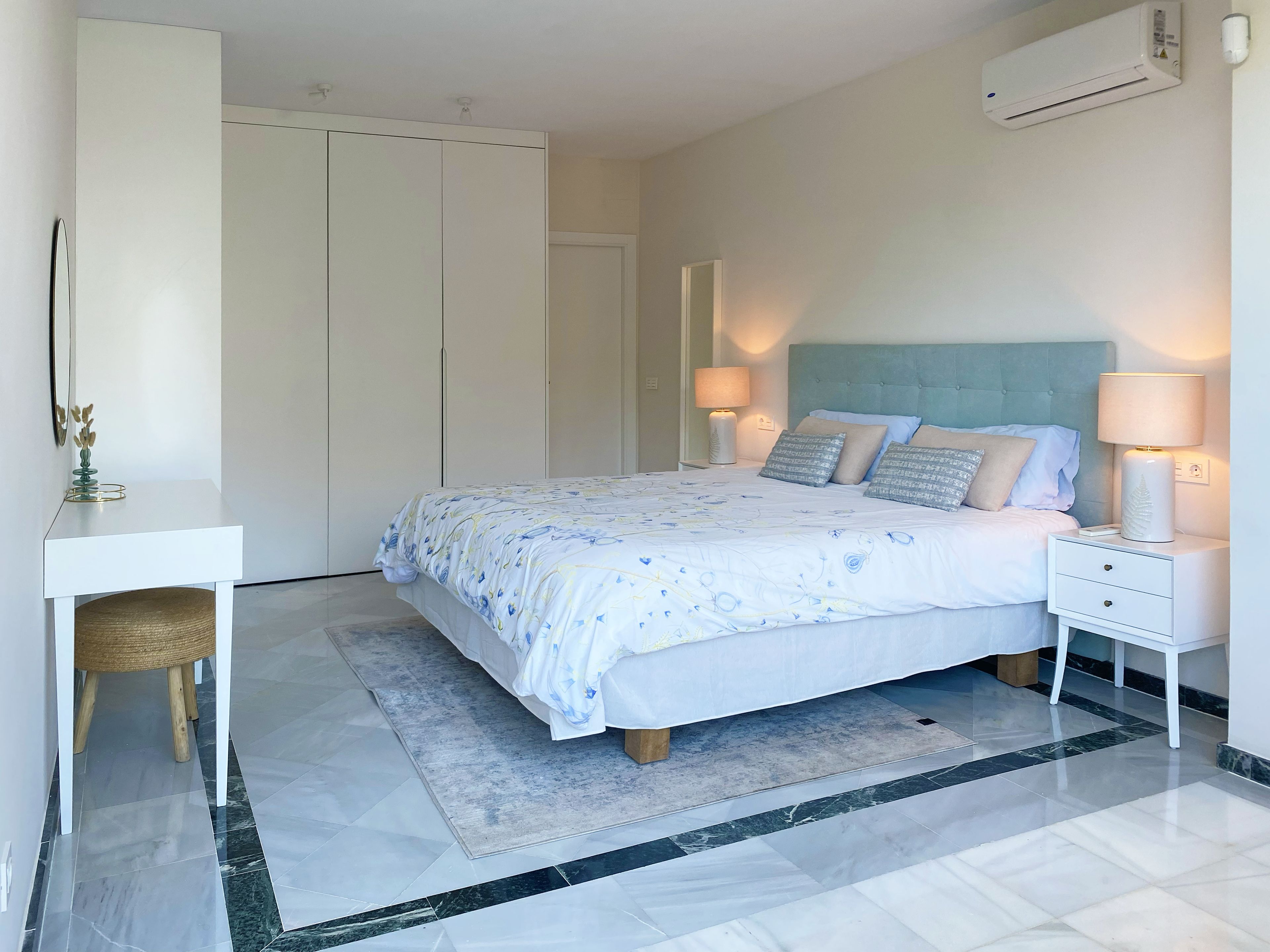 A bedroom with a bed, bedside tables, a desk, and an air conditioning unit.
