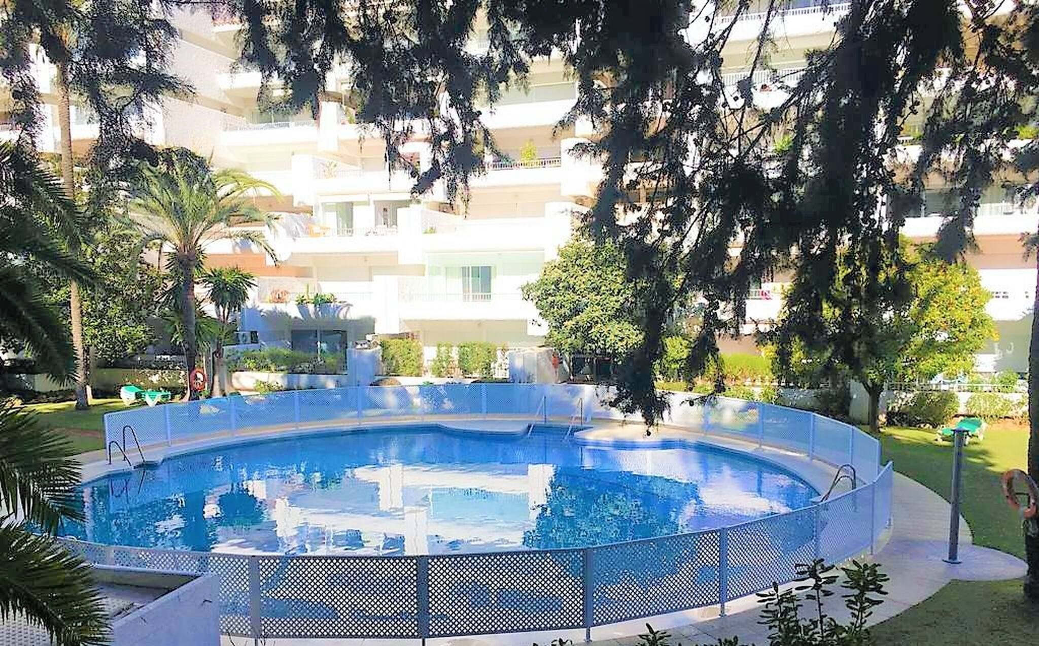 Ein runder Pool mit blauem Zaun, umgeben von Grünflächen und Wohnhäusern im Hintergrund.