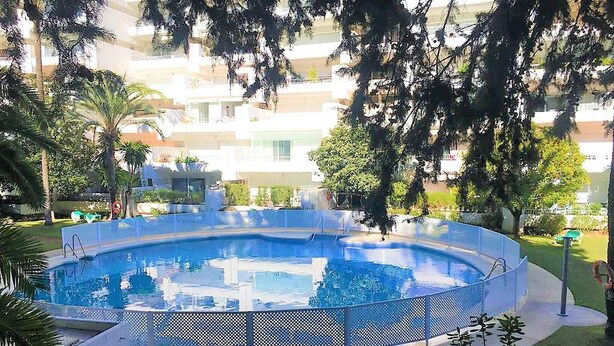 Ein runder Pool mit blauem Zaun, umgeben von Grünflächen und Wohnhäusern im Hintergrund.