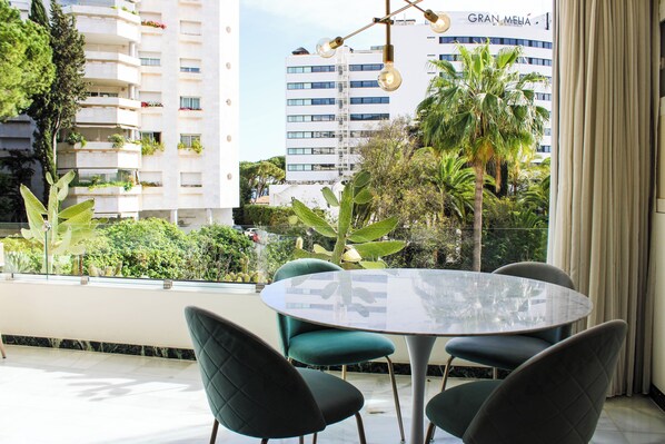 A modern outdoor dining area with a round glass table and dark green chairs, overlooking a cityscape with a prominent building labeled "GRAN MELIA". - Fantastic Apartment 2 Minutes Walk From The Beach (Marbella)