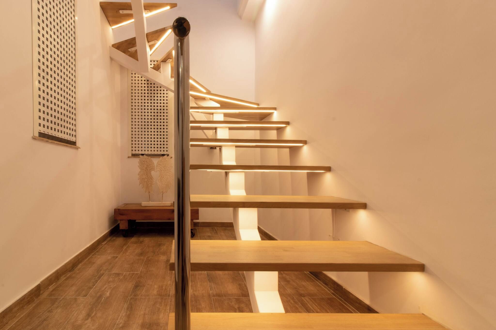A modern staircase with wooden steps and a metal handrail, leading to a landing with a decorative wall piece.