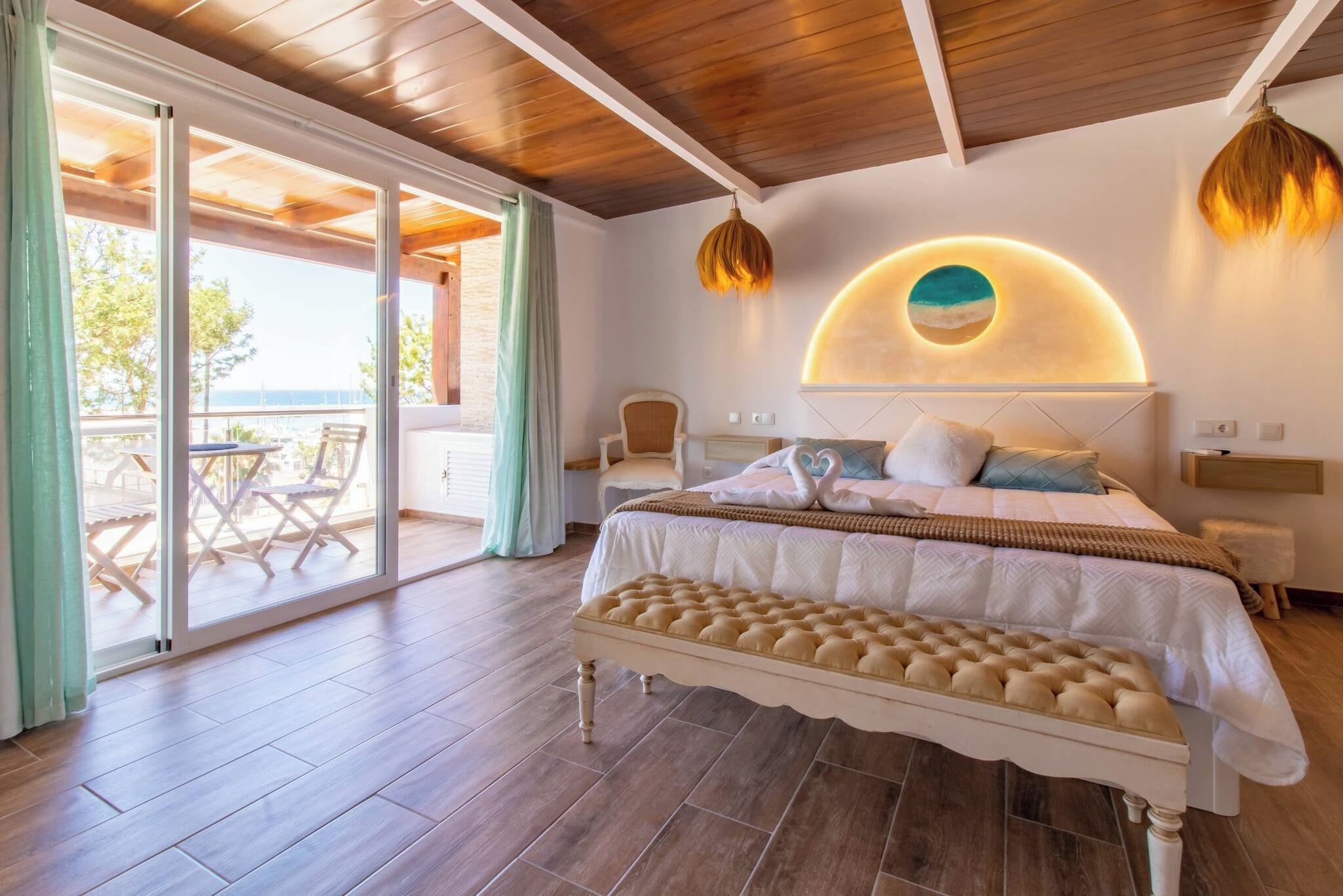 A bedroom with a large bed, a bench, a circular wall decoration, and a view through a glass door to an outdoor area.