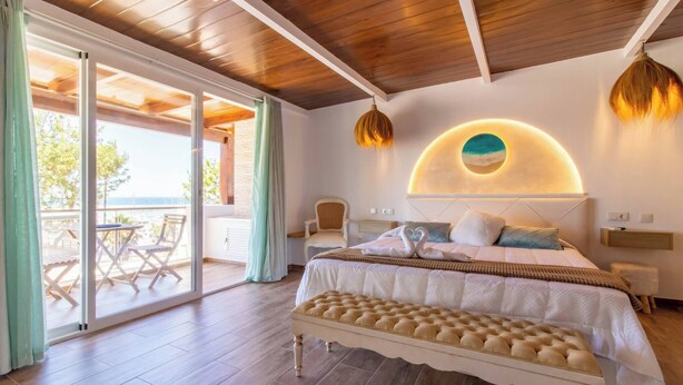 A bedroom with a large bed, a bench, a circular wall decoration, and a view through a glass door to an outdoor area. - Room in Guest Room - Private Room With Beautiful sea View (Marbella)