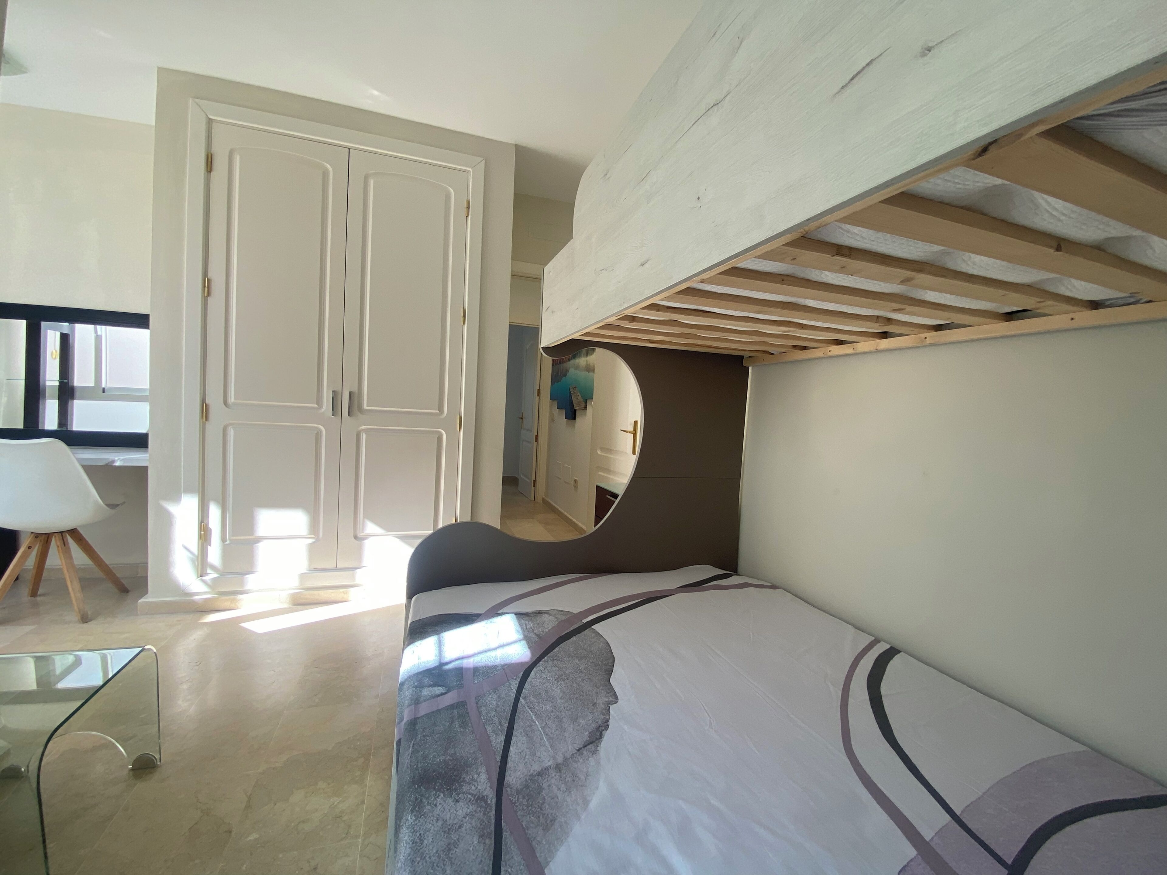 A bedroom with a bed, a wardrobe, a mirror, and a desk with a chair.