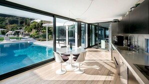 Une cuisine moderne dotée d’une grande fenêtre donnant sur une piscine et une végétation luxuriante.