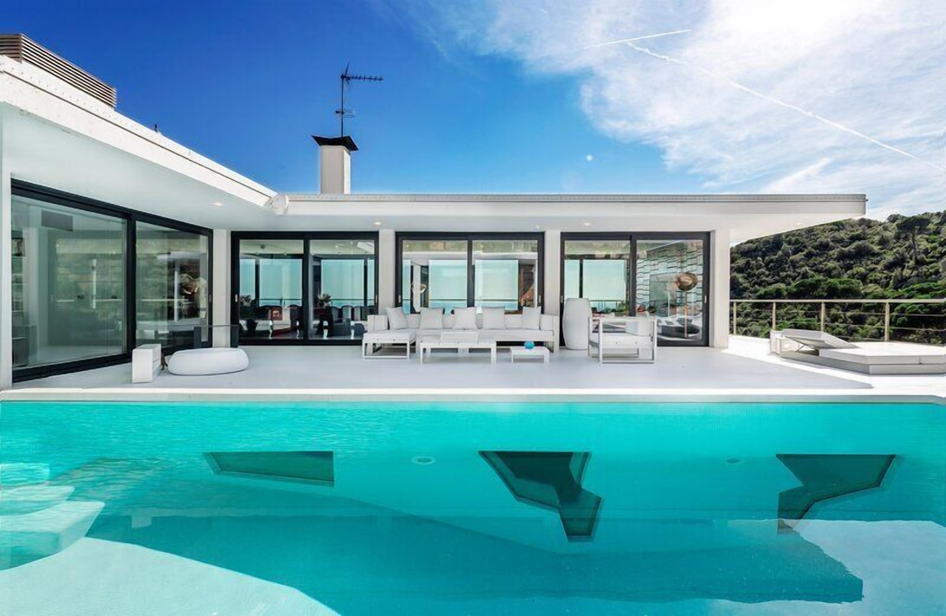 A modern house with a large swimming pool, outdoor seating area, and a view of a hill.