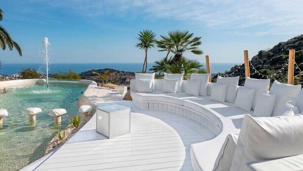 Un espace extérieur luxueux, aménagé avec des sièges confortables, une piscine, des coussins blancs et une vue dégagée sur l’océan.