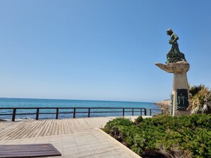 Uma estátua em um pedestal à beira-mar, uma passarela de madeira e um corrimão.