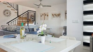 A modern living room with a white dining table, a sofa, and a staircase. - The Fairways - Luxurious Front Line Villa on Mar Menor Golf Resort (Torre-Pacheco)