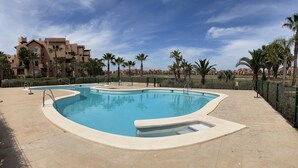 A swimming pool with a curved design, surrounded by a tiled deck. - The Fairways - Luxurious Front Line Villa on Mar Menor Golf Resort (Torre-Pacheco)