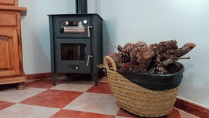 A room with a black wood-burning stove, a woven basket of firewood, and a wooden cabinet. - La Reconquista, Despeñaperros (Santa Elena)