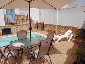 A glass-top table with chairs, a pool, a stone wall, and a grill. - La Reconquista, Despeñaperros (Santa Elena)