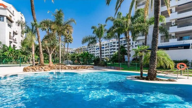 A swimming pool surrounded by palm trees and a building with balconies.