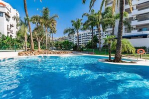 A swimming pool surrounded by palm trees and a building with balconies. - Beautiful 2 Bedrooms Apartment In Puerto Banus (Marbella)