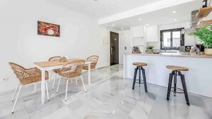 A modern kitchen with white cabinetry, a central island with stools, and a dining area with wicker chairs.